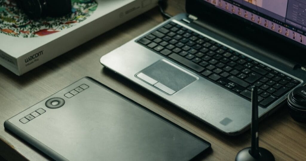 Modern digital artist setup with laptop, tablet, and stylus on desk.