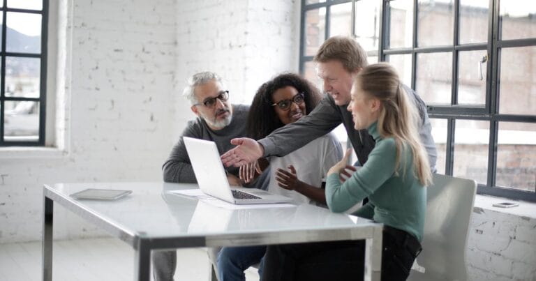 A diverse team of professionals discussing a project around a laptop in a modern office setting.