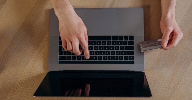 Top view of hands using a credit card and laptop for online transactions on a wooden surface.