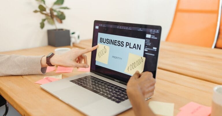 Hands collaborate on a business plan with a laptop in a modern office setting.