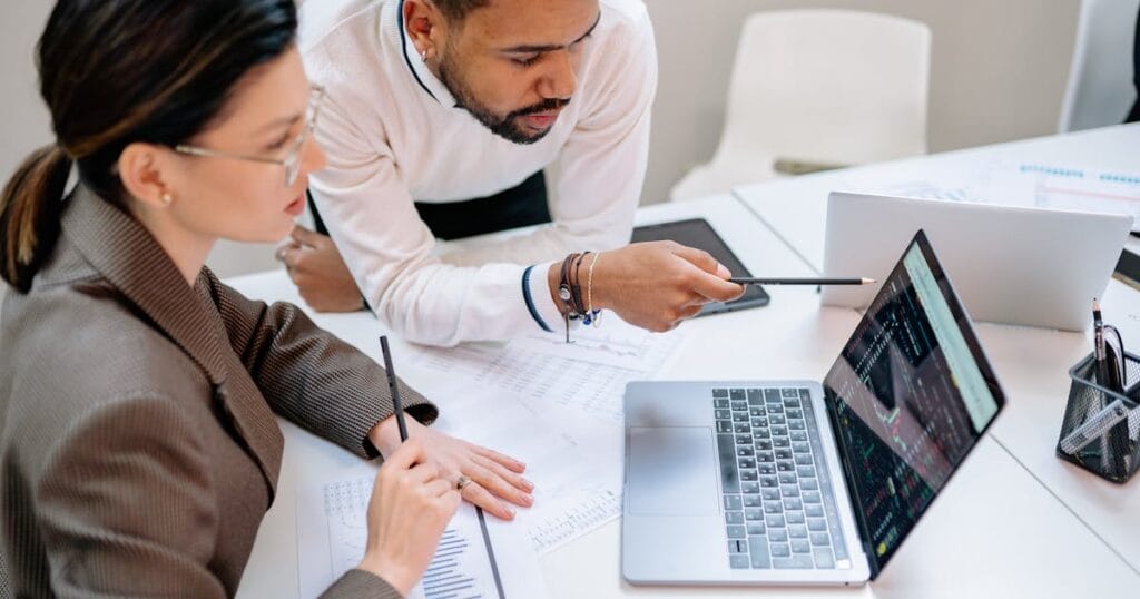 Business professionals discussing data at a desk with a laptop.